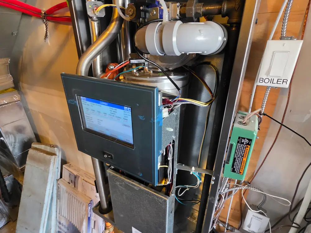 High-efficiency boiler opened for commissioning, showing the control display and primary piping